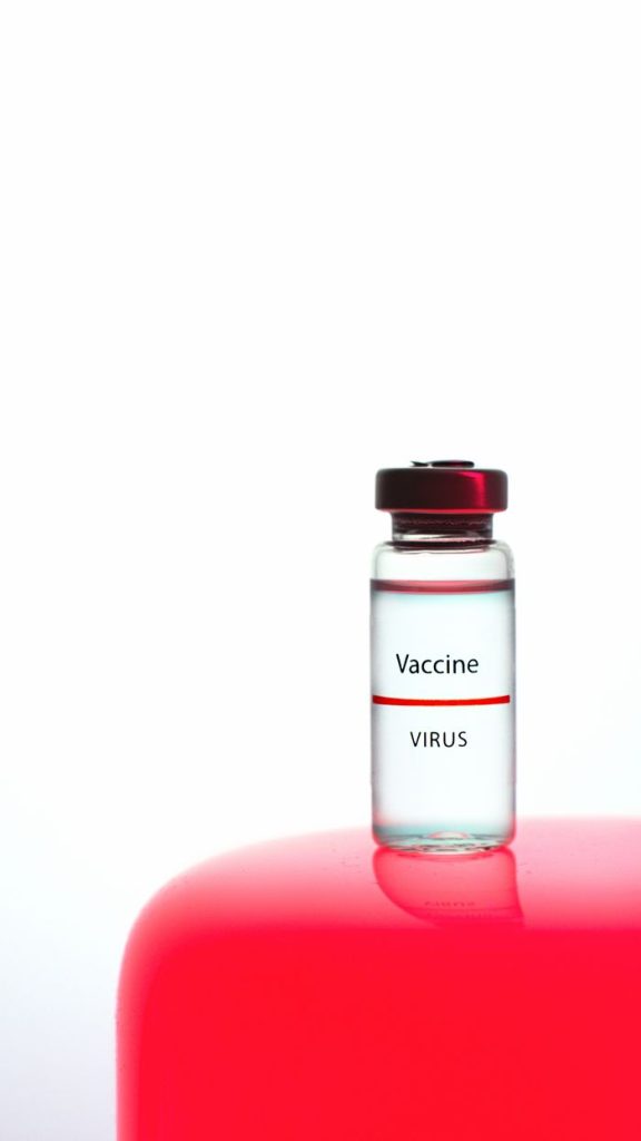 Close-up of a vaccine vial labeled 'Vaccine Virus' on a striking red and white background.