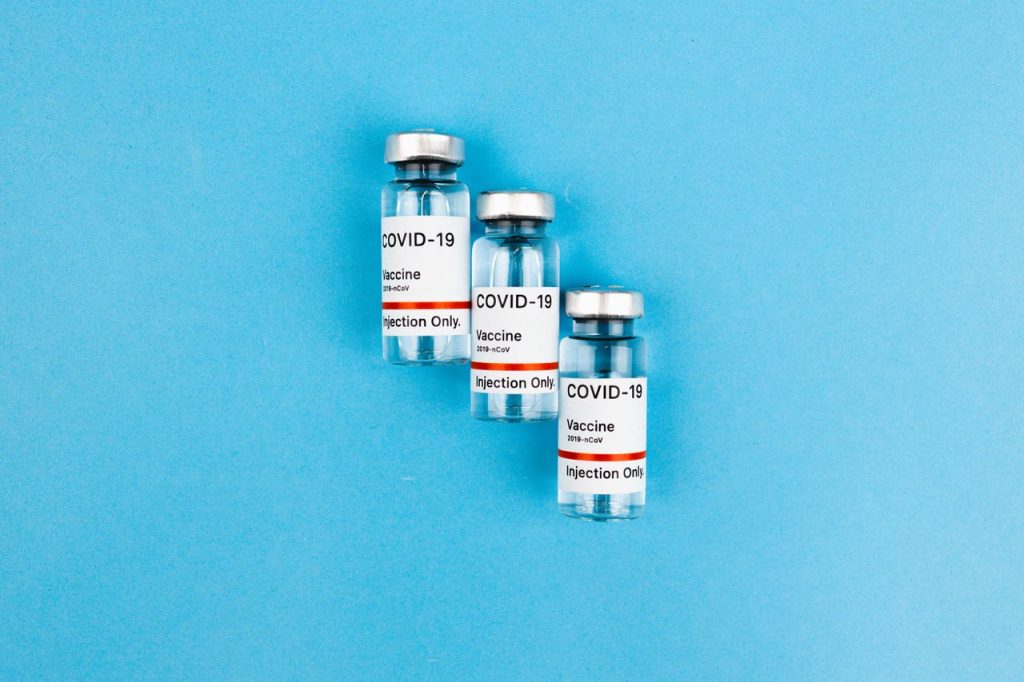 Three COVID-19 vaccine vials with labels on a bright blue background.
